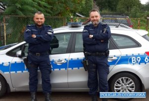 Dwóch umundurowanych policjantów stoi na dworze na tle oznakowanego radiowozu