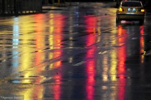 Droga w czasie deszczu. W tle kolorowe światła odbijające się od nawierzchni asfaltowej