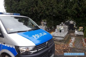 Policyjny radiowóz a w tle nagrobki cmentarne