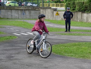 dziewczynka jedzie rowerem, za nią stoi policjant