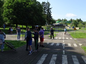 chłopiec jedzie rowerem sygnalizując ręką skręt w prawo przed nim stoi grupka dzieci policjant z policjantką