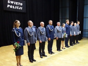 10 policjantów w mundurach po wręczeniu medali, stoją w szeregu na scenie.