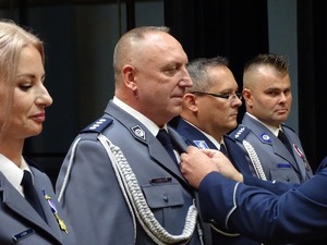 trzech policjantów w mundurach galowych i jedna policjantka, stojącemu w środku przypinany jest medal za zasługi