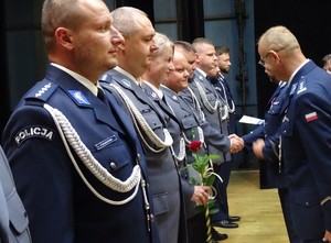 w szeregu stoją policjanci, jednemu z nich stojący na przeciwko komendant podaje rękę wręczając odznaczenia, wszyscy mają założone mundury galowe