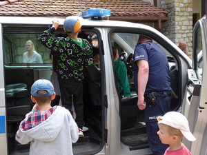 w radiowozie oznakowanym znajduje się czwórka dzieci przy nich stoi policjant w mundurze, dwoje dzieci stoi przed radjowozem