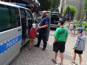 z boku radiowozu stoi policjant oraz czterech chłopców