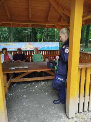 pod wiatą stoi policjantka w mundurze na ławce siedzą trzy kobiety - seniorki