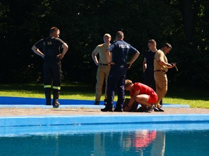 na basenie znajduje się policjant oraz czterech strażaków wszyscy umundurowani, ratownik otwiera klapkę od przepompowni