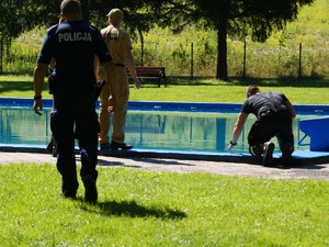 na basenie umundurowani, strażacy, policjant, jeden ze strażaków wkłada rękę do wody znajdującej się w basenie