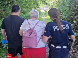 Starsza kobieta jest prowadzona jest policjantkę i ratownika medycznego