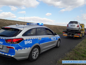 Na prawym pasie jezdni stoi oznakowany radiowóz a przednim laweta, na której stoi samochód osobowy marki skoda