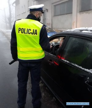 Policjant z żółtą kamizelką z napisem POLICJA, bada stan trzeźwości kierującego pojazdem