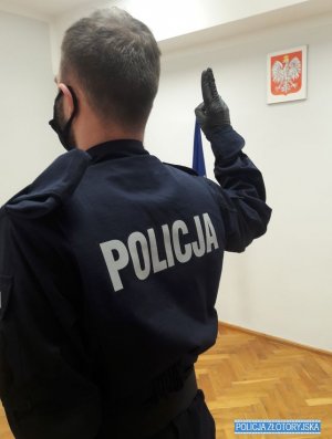 Policjant z dłonią uniesioną do góry, w tle godło Polski