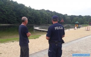 Dwie osoby, w tym policjant stoją na brzegu kąpieliska